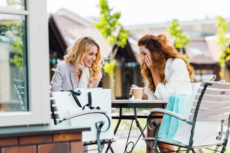 happy young women sitting in cafe together after shoppingの写真素材