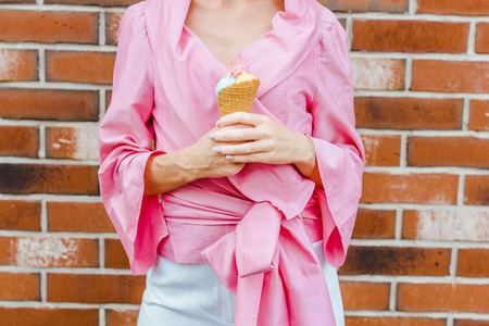 cropped shot of woman in pink holding ice cream in front of brick wallの写真素材