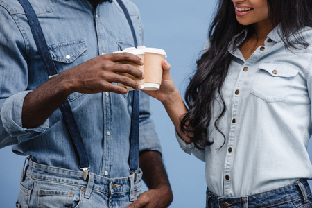 cropped image of african american couple clinking with coffee in paper cups isolated on blueの写真素材