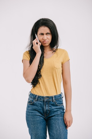 irritated african american girl talking by smartphone isolated on whiteの写真素材