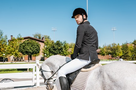 handsome male equestrian in professional apparel sitting on horseback at horse clubの写真素材
