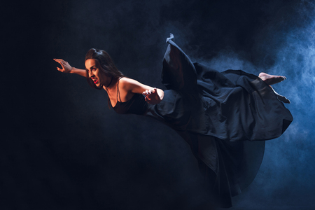 grim woman in vampire costume flying on darkness with smokeの写真素材