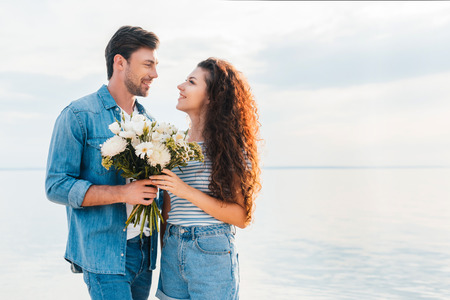 happy couple hugging and holding bouquet near the seaの写真素材