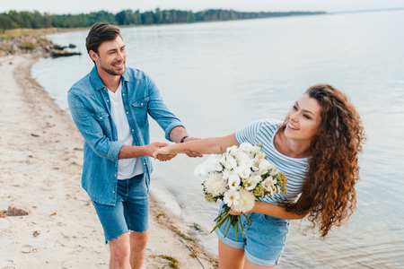 beautiful happy girlfriend with bouquet holding hands with boyfriendの写真素材