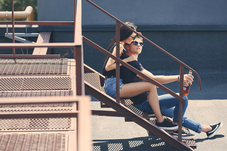 multiethnic couple with bottle of whiskey hugging and sitting on stairs on roofの写真素材