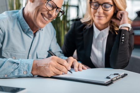 smiling adult customer signing contract with female car dealer at showroom