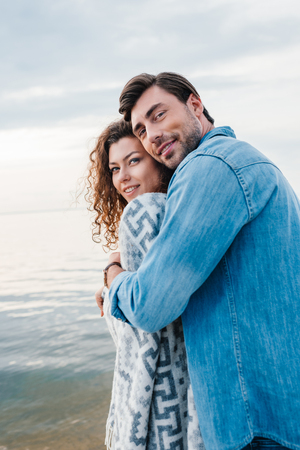 happy man hugging girlfriend wrapped in blanketの写真素材