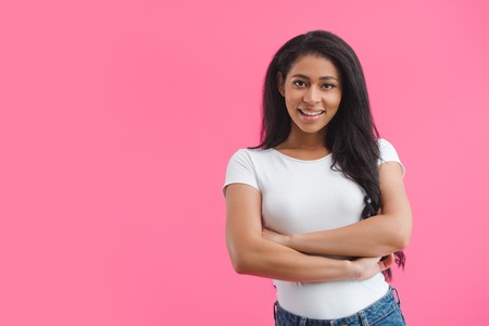 portrait of smiling african american woman with arms crossed isolated on pinkの写真素材