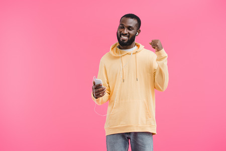 happy african american man in earphones gesturing by hand listening music with smartphone isolated...