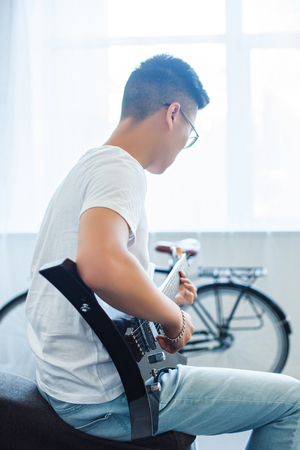 side view of asian man playing unplugged electric guitar at homeの写真素材