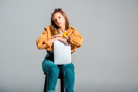 bored girl with laptop sitting on stool isolated on greyの写真素材
