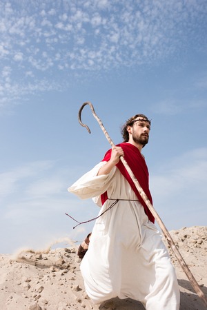 Jesus in robe, red sash and crown of thorns running in desert with staffの写真素材