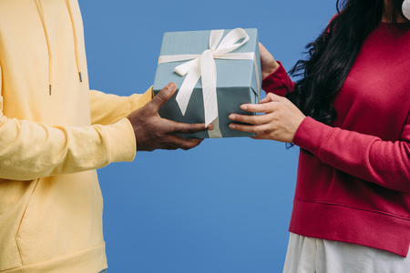 cropped image of man presenting gift box wrapped by ribbon to girlfriend isolated on blue background
