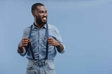 stylish young african american man touching suspenders isolated on blue backgroundの写真素材