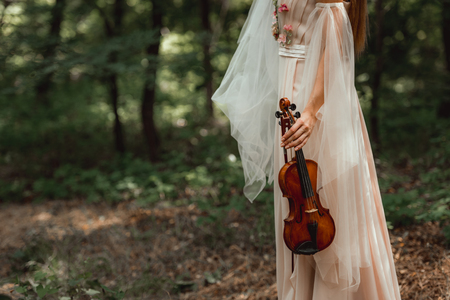 cropped view of girl in dress with flowers holding violin in woodsの写真素材