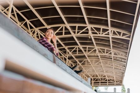 low angle view of attractive cowgirl in checkered shirt sitting on bench at ranch stadiumの写真素材