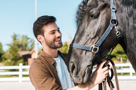smiling handsome cowboy fixing horse halter at horse clubの写真素材