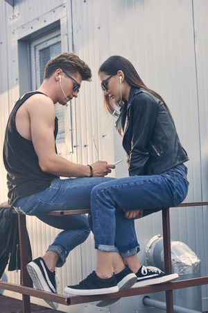 young multiethnic couple listening music with earphones and using smartphone togetherの写真素材
