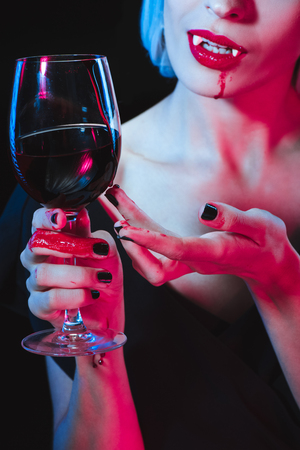 cropped view of vampire holding wineglass with blood isolated on blackの写真素材