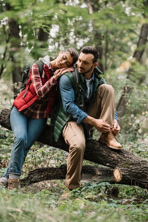 young travelers resting on log while hiking in forestの写真素材