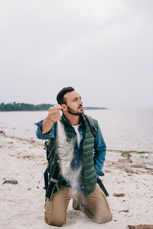 man with backpack pouring sand on beachの写真素材