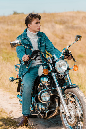 handsome stylish young man sitting on vintage motorbike on rural meadowの写真素材
