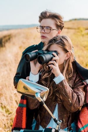 girlfriend looking through binoculars near handsome boyfriend sitting on motorbikeの写真素材