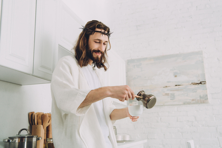 cheerful Jesus pouring coffee from cezve into cup in kitchen during morning time at homeの写真素材