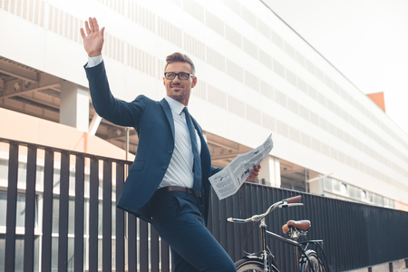 low angle view of smiling businessman holding newspaper and waving hand on streetの写真素材