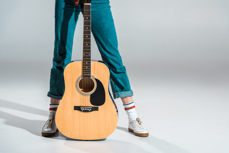 cropped view of girl in jeans posing with acoustic guitar on greyの写真素材
