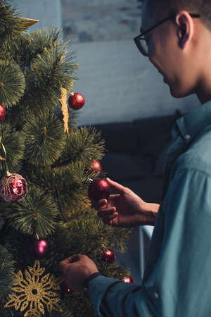 cropped shot of young asian man in eyeglasses decorating christmas tree at homeの写真素材