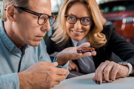 close-up shot of adult man and smiling female car dealer looking at toy car in showroomの写真素材