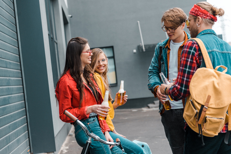 happy friends with bicycle drinking beer from bottles on streetの写真素材