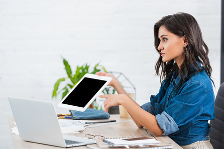 side view of young woman pointing on digital tablet with blank screen at tableの写真素材
