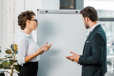 side view of business colleagues discussing work at blank white board in officeの写真素材