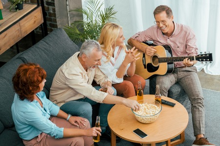 high angle view of happy old friends spending time with guitar and beer at homeの写真素材
