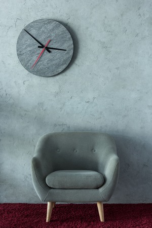 grey armchair on burgundy carpet near grey wall in office, clock on wall