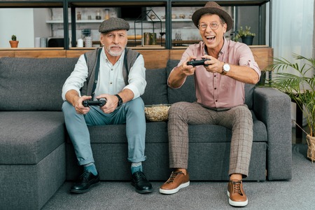 handsome mature men sitting on sofa and playing with joysticks