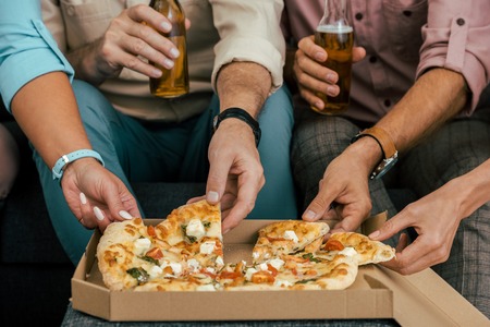 cropped shot of mature friends drinking beer and eating pizza togetherの写真素材