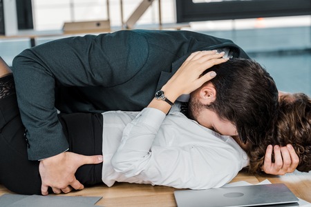passionate businessman and businesswoman lying on table in officeの写真素材