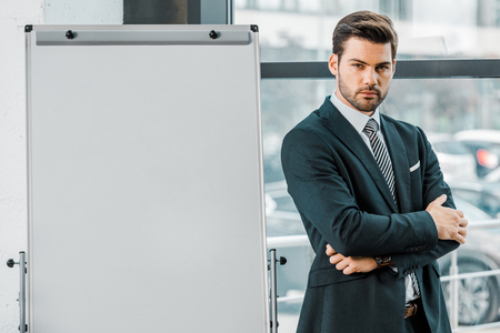 portrait of confident businessman in suit standing at empty white board in officeの写真素材