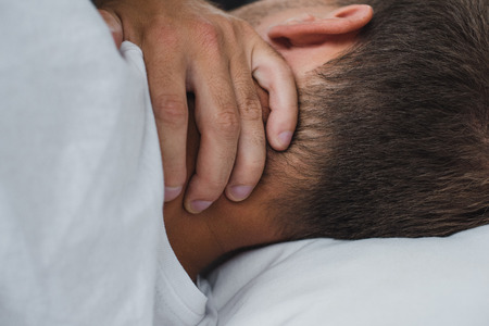 close-up view of man suffering from pain in neck while lying on bedの写真素材