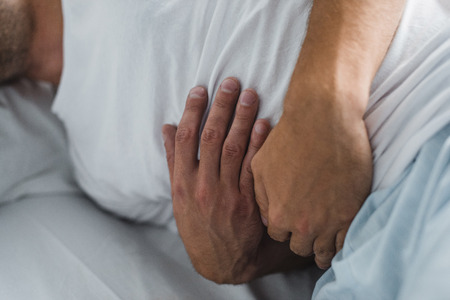 close-up partial view of man suffering from stomach pain in bedの写真素材