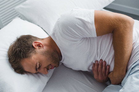 high angle view of man lying in bed and suffering from stomach painの写真素材