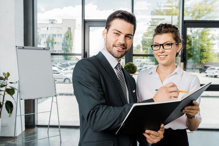 portrait of smiling businessman signing papers with colleague near by  in officeの写真素材