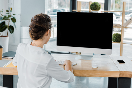 back view of businesswoman working on computer with blank screen in officeの写真素材