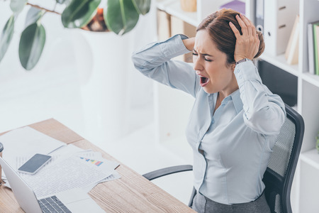 high angle view of stressed businesswoman holding her head and screaming at workplaceの写真素材