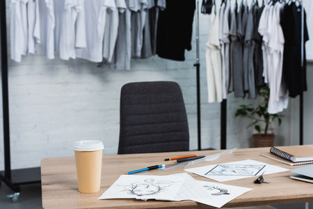 selective focus of coffee cup and paintings on working table in clothing design studioの写真素材