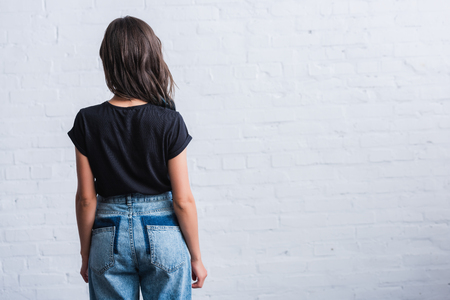 rear view of young woman in empty black t-shirt in front of brick wallの写真素材
