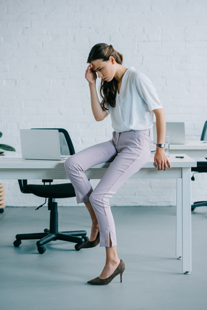 young businesswoman sitting on table and suffering from headache in officeの写真素材